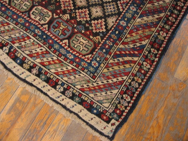 Intricate geometric rug corner featuring red, blue, black, and cream motifs on distressed wood planks.