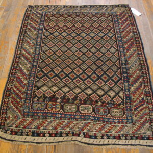 Black rug with repeating colored diamond medallions and borders sits on distressed wood floor.