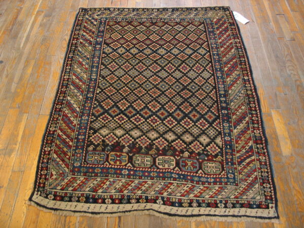 Black rug with repeating colored diamond medallions and borders sits on distressed wood floor.
