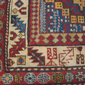 Woven rug detail showing tight geometric patterns in vibrant red, bright blue, cream, and mustard yellow.