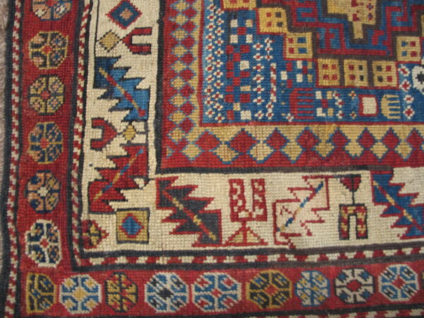Woven rug detail showing tight geometric patterns in vibrant red, bright blue, cream, and mustard yellow.