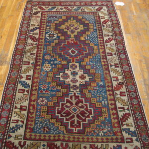 Red, blue, and gold geometric low-pile rug with tribal motifs displayed on light wood flooring.