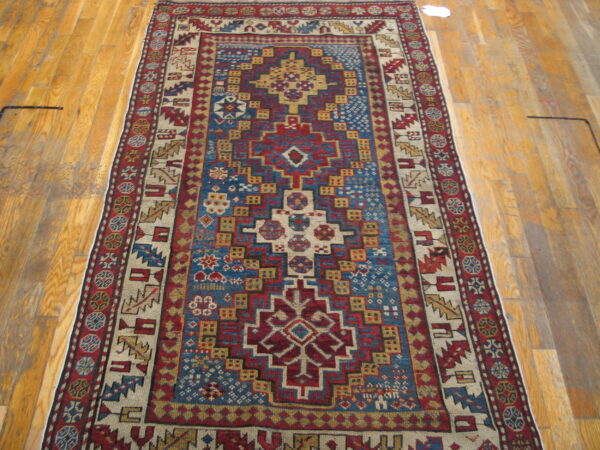 Red, blue, and gold geometric low-pile rug with tribal motifs displayed on light wood flooring.