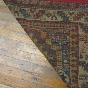 Geometric red, blue, and gold flatweave rug shown covering a section of distressed light hardwood flooring.