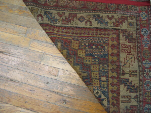Geometric red, blue, and gold flatweave rug shown covering a section of distressed light hardwood flooring.