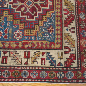 Low-pile rug corner featuring bold geometric motifs in blue, red, and gold on wood planks.
