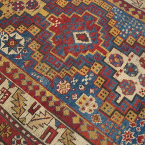 Close-up of a geometric rug featuring complex tribal patterns in red, blue, gold, and cream.