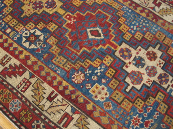 Close-up of a geometric rug featuring complex tribal patterns in red, blue, gold, and cream.