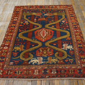 Pictorial rug with rust, navy, and gold colors features a central serpentine motif on rustic wood flooring.