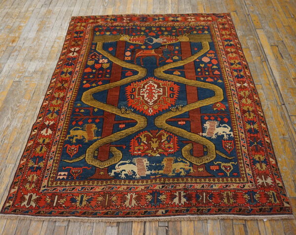 Pictorial rug with rust, navy, and gold colors features a central serpentine motif on rustic wood flooring.