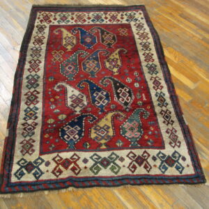Red rug with geometric boteh patterns in blue and gold sits on light-colored plank flooring.