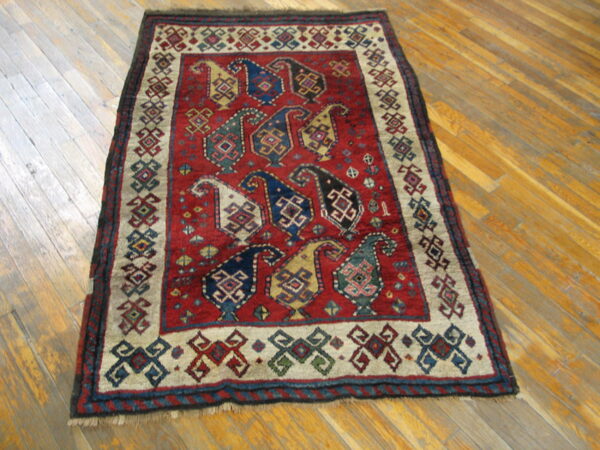 Red rug with geometric boteh patterns in blue and gold sits on light-colored plank flooring.