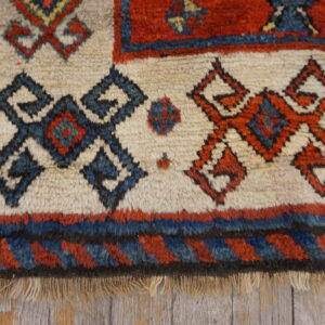 Cream high-pile rug detail showing red and navy geometric tribal motifs against weathered wood flooring.