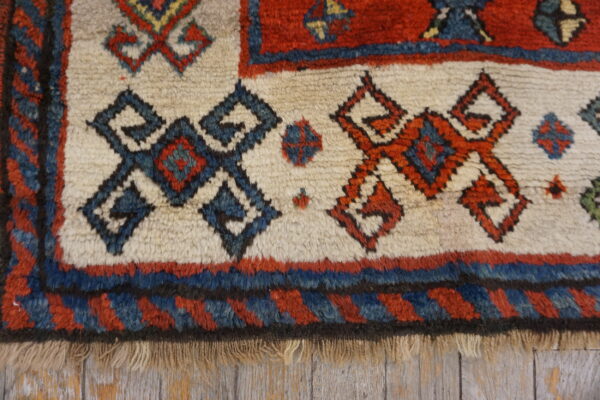 Cream high-pile rug detail showing red and navy geometric tribal motifs against weathered wood flooring.