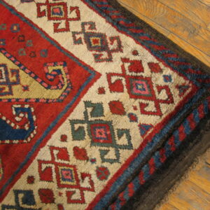 Red, cream, and blue geometric rug corner shows thick pile over light brown wood planks.