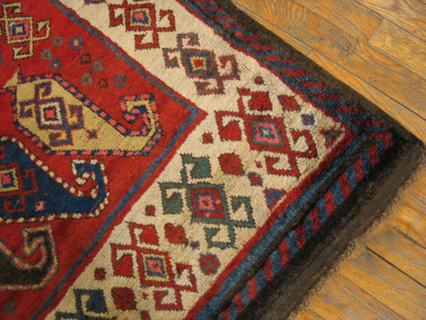 Red, cream, and blue geometric rug corner shows thick pile over light brown wood planks.