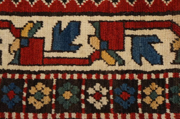 Detailed view of rug borders featuring dense pile and stylized floral and geometric motifs in red, cream, blue, and yellow.