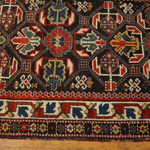 Dark geometric rug featuring bold red, blue, and cream medallions rests on a light wood floor.