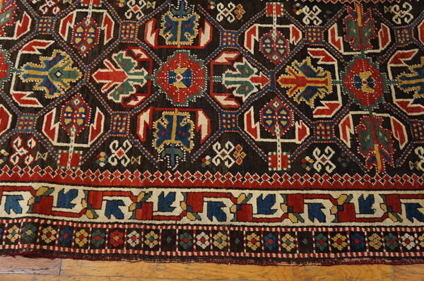 Dark geometric rug featuring bold red, blue, and cream medallions rests on a light wood floor.
