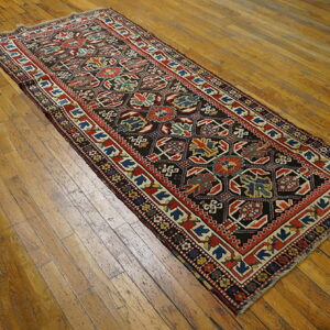 Geometric runner rug with a dark field, red borders, and multi-colored motifs on distressed wood plank flooring.