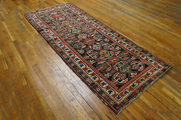 Geometric runner rug with a dark field, red borders, and multi-colored motifs on distressed wood plank flooring.