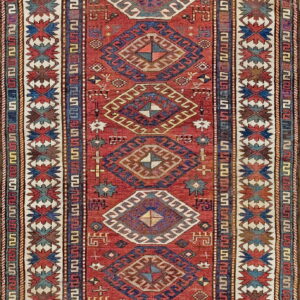 Red field rug with stacked multicolored geometric diamonds and a wide cream border of zigzag star motifs.