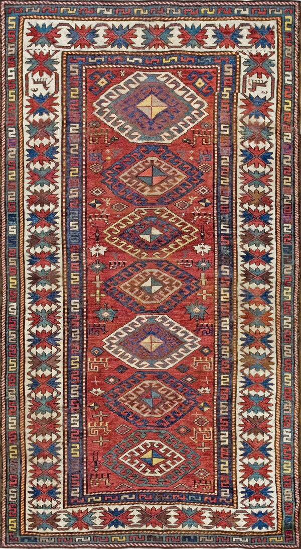 Red field rug with stacked multicolored geometric diamonds and a wide cream border of zigzag star motifs.