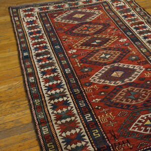 Red runner rug with stacked diamond geometric motifs and complex borders on wooden planks.