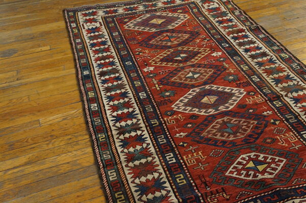 Red runner rug with stacked diamond geometric motifs and complex borders on wooden planks.