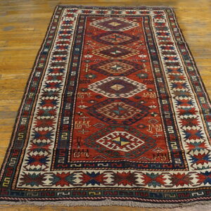 Red runner rug with geometric diamond medallions and navy borders lies on polished wood flooring.