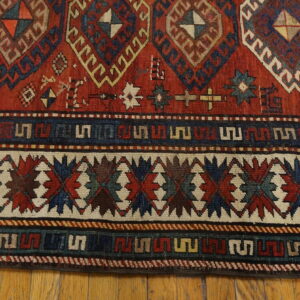 Tightly woven rug in red, blue, and cream tribal patterns resting on natural hardwood flooring.