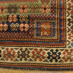 Geometric rug with rust, navy, olive, and cream patterns lies on distressed light wooden planks.