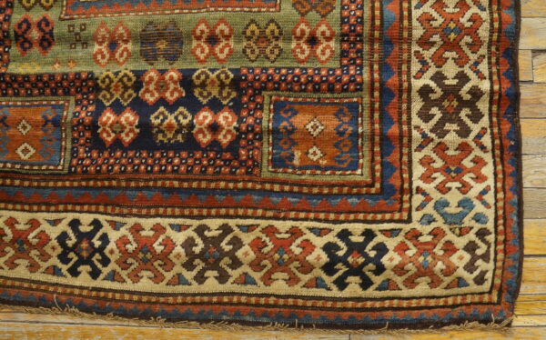 Geometric rug with rust, navy, olive, and cream patterns lies on distressed light wooden planks.