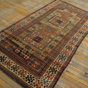 A richly patterned low-pile rug in green, blue, and terracotta sits on distressed wooden floors.