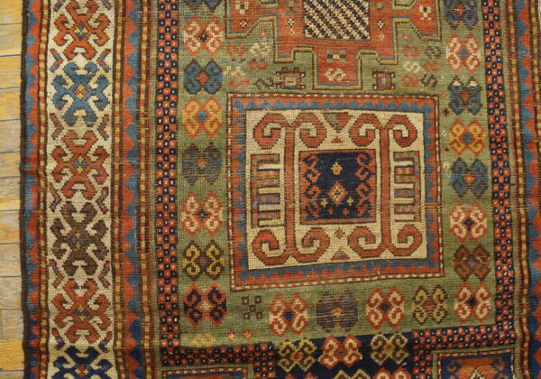 Detailed view of a low-pile rug with geometric patterns in olive green, rust, and blue on wood planks.