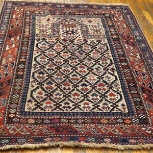 Geometric tribal-style rug in red, blue, and cream colors is displayed on glossy light brown wood floorboards.