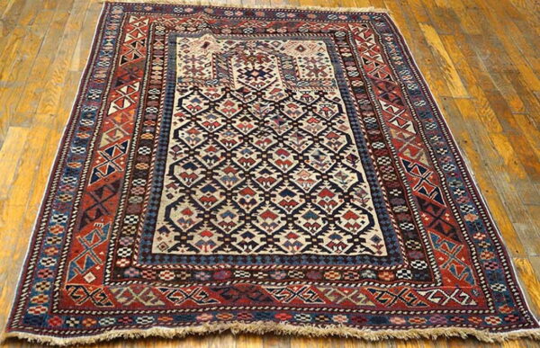 Geometric tribal-style rug in red, blue, and cream colors is displayed on glossy light brown wood floorboards.