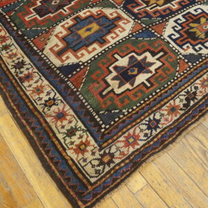 Low-pile rug with geometric patterns in red, navy, green, and cream on light wood flooring.