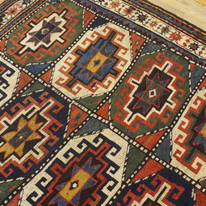 Diagonal view of a colorful geometric rug with repeating diamond medallions on pale wood planks.