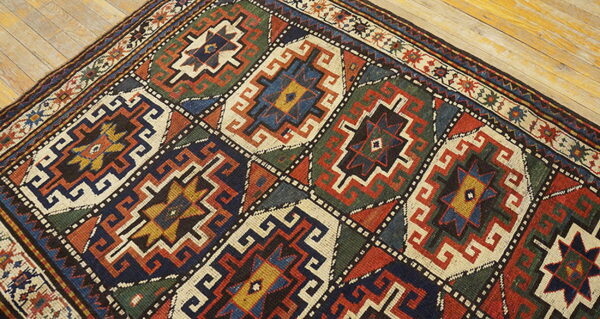 Diagonal view of a colorful geometric rug with repeating diamond medallions on pale wood planks.