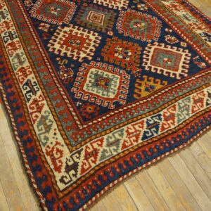 Angled view of a blue and red geometric rug featuring large medallions and intricate borders on worn plank flooring.