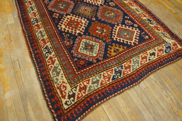 Angled view of a blue and red geometric rug featuring large medallions and intricate borders on worn plank flooring.