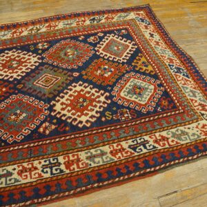 Detailed geometric rug in indigo, red, cream, and gold displayed on wide plank rustic flooring.