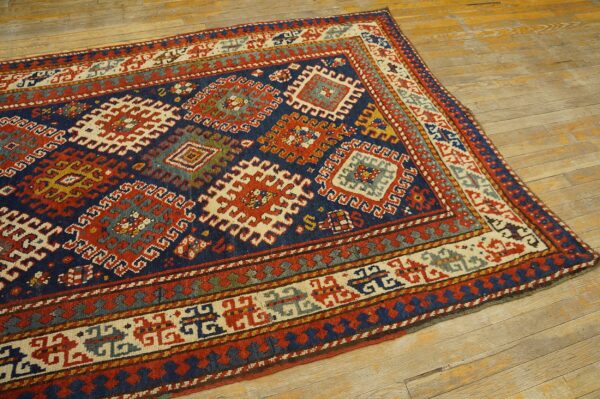 Detailed geometric rug in indigo, red, cream, and gold displayed on wide plank rustic flooring.