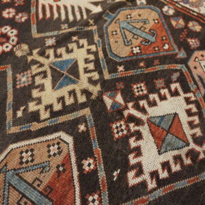 Dark brown rug surface with angular geometric patterns in deep red, cream, blue, and tan colors.