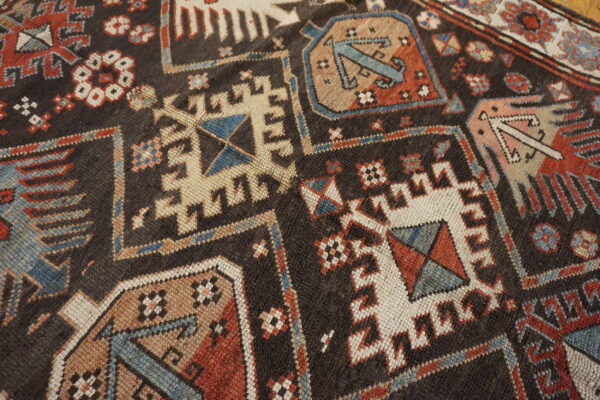 Dark brown rug surface with angular geometric patterns in deep red, cream, blue, and tan colors.