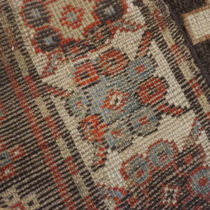 Close-up of a dense rug showing geometric patterns in brown, cream, red, and light blue.
