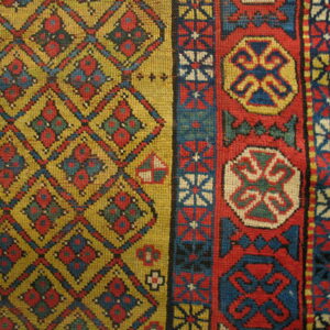 Geometric rug detail showing a yellow diamond lattice field and a wide red, blue, and cream patterned border.
