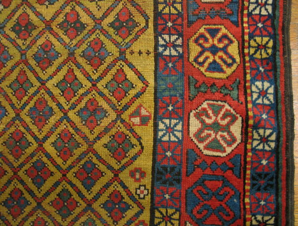 Geometric rug detail showing a yellow diamond lattice field and a wide red, blue, and cream patterned border.