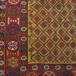 Low-pile geometric rug with a golden yellow diamond field and thick red, blue, and white border on wood flooring.